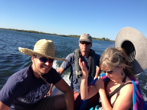 2 men and 1 woman in a small boat, woman's hat is blowing off her head